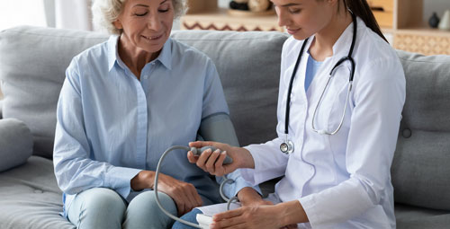 An elderly woman being visited by a doctor at home she is receiving a blood pressure test